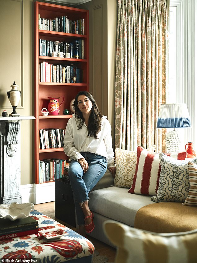 The sofa is stacked with cushions made of salvaged fabrics from Haines, including examples by Nicky Haslam and Susie Atkinson. The curtains and the covering on the ottoman are also from Haines